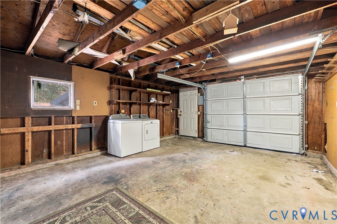 Garage space featuring exposed timber ceiling joists, panelled wood-finish wall detailing, integrated wall-mounted shelving, a sectional roll-up door, and laundry hookups