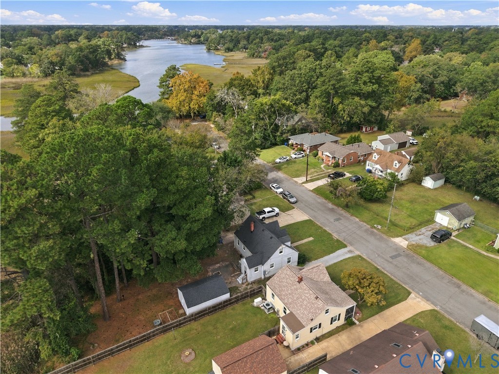 Aerial perspective featuring wooded surroundings, residential lots, asphalt street, and a proximity to tidal waterways