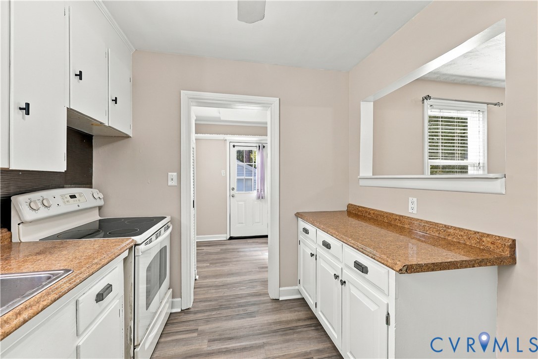 Kitchen featuring white cabinetry, stone-finish countertops, an integrated pass-through window, and wood-finish flooring
