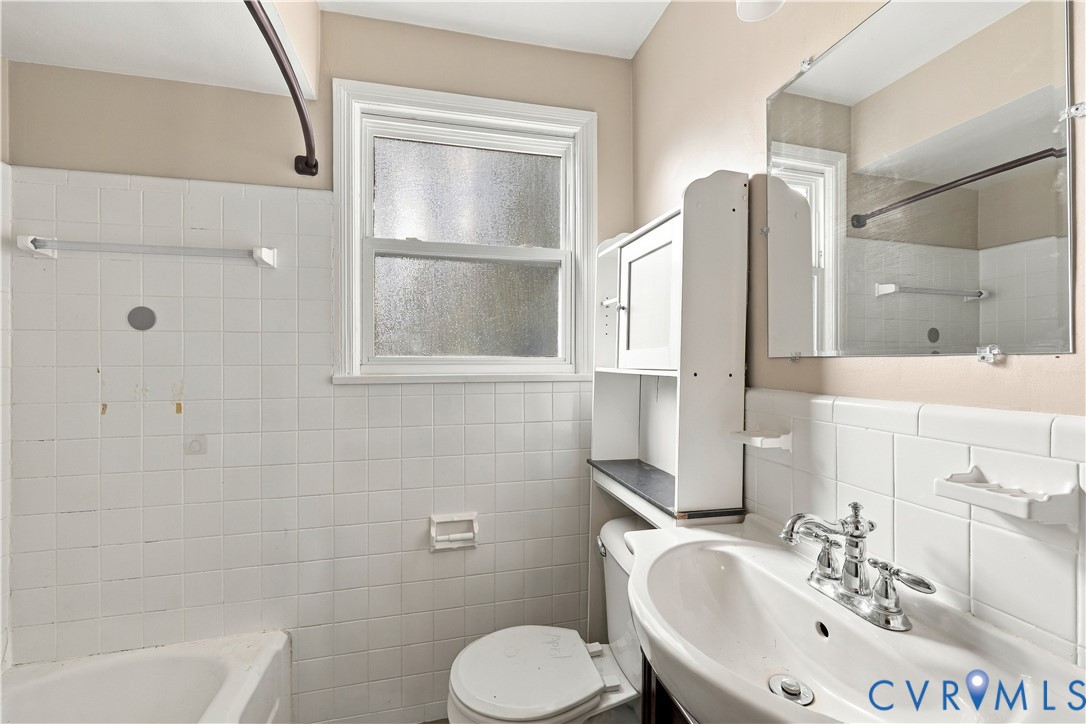 Bathroom featuring white wall tiling, a pedestal sink with chrome faucet hardware, built-in medicine cabinet shelving, and a single-hung window with privacy glass