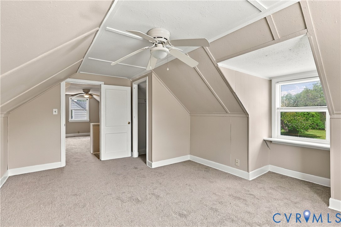 Interior room featuring sloped ceilings, wall-to-wall carpeting, a ceiling fan with integrated lighting, and dual-pane windows