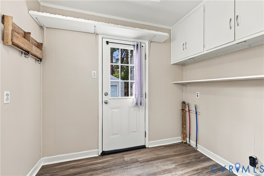 Utility room featuring wood-finish flooring, white overhead cabinetry, wall-mounted shelving, a wood-finish wall rack, and an exterior door with glass panes