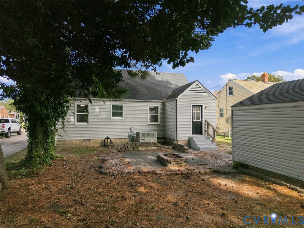 Exterior featuring light-toned vinyl siding, a paver patio, a built-in stone fire pit, and a detached structure