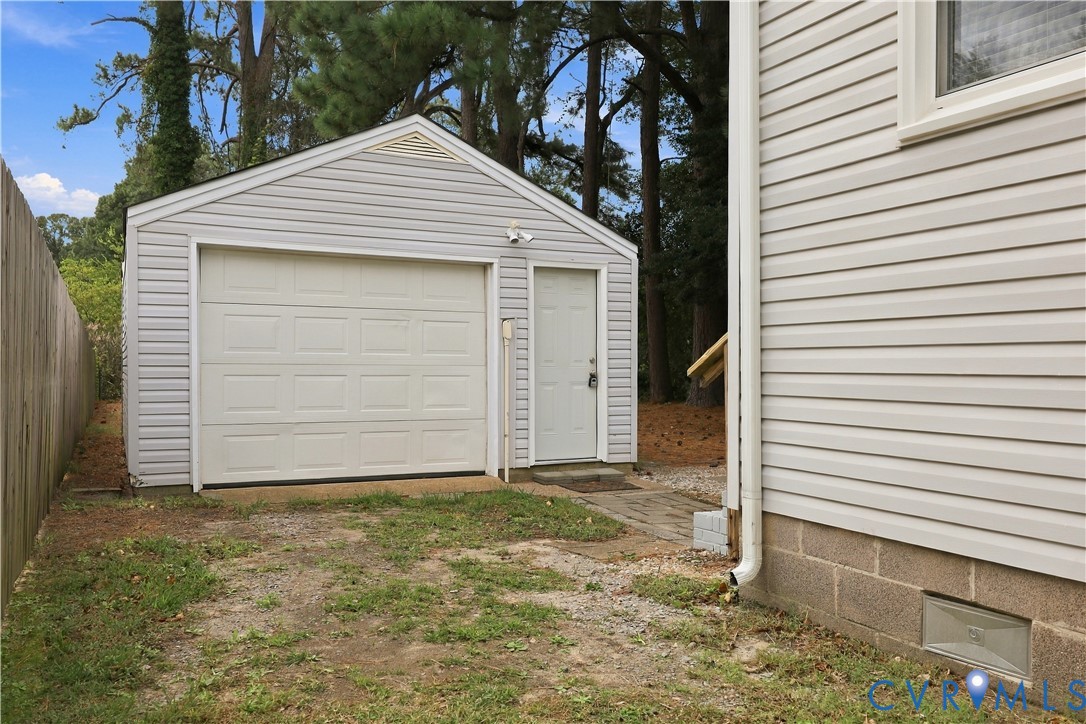 Detached single-car garage featuring light-colored vinyl siding, a white roll-up garage door, a side entry door, and a concrete block foundation