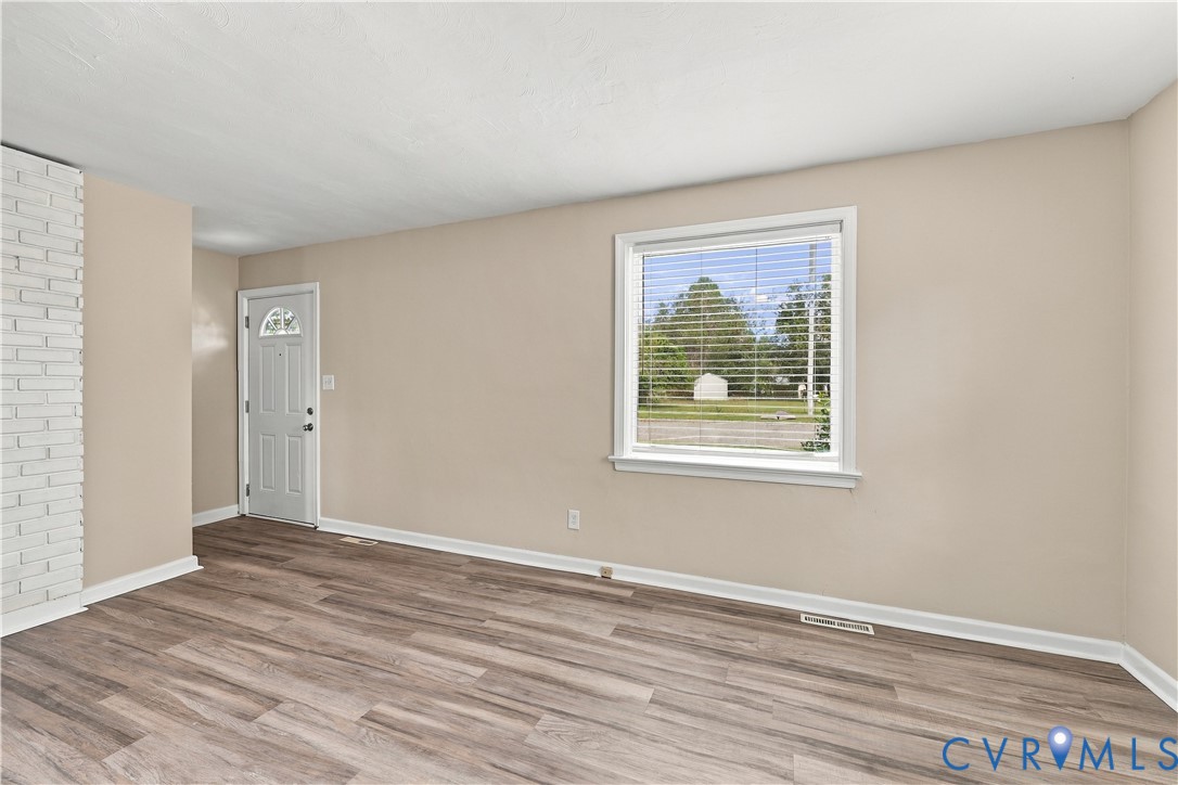 Living area featuring wood-finish flooring, a painted brick fireplace surround, and a single-lite paneled exterior door
