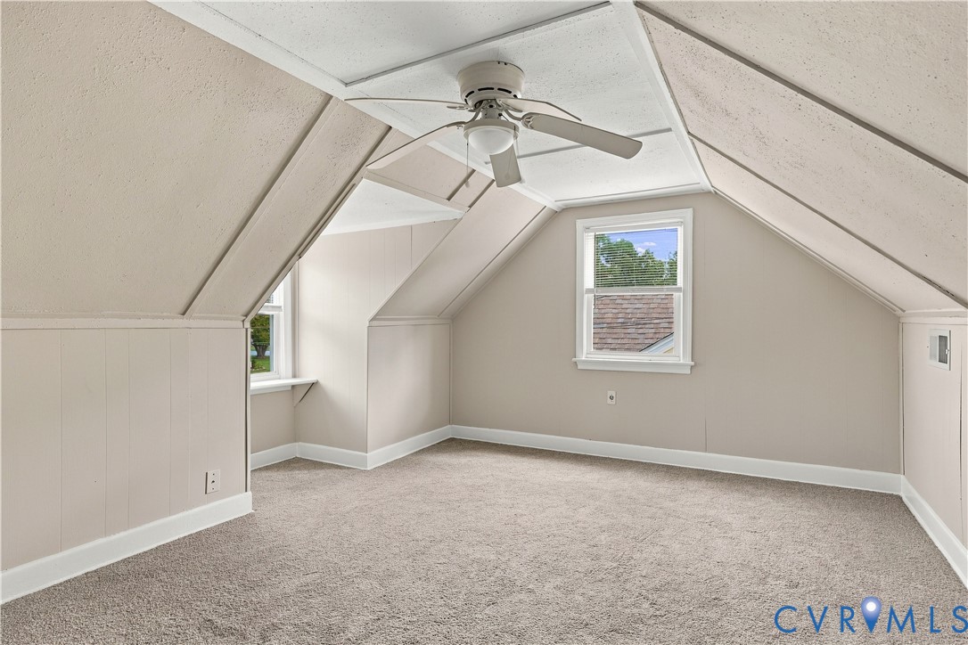 Attic space featuring slanted walls, dual windows, neutral carpeting, and a ceiling-mounted fan