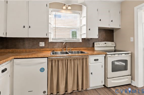 Kitchen featuring white shaker-style cabinetry, solid-surface countertops, dual-basin stainless steel sink, and wood-finish flooring