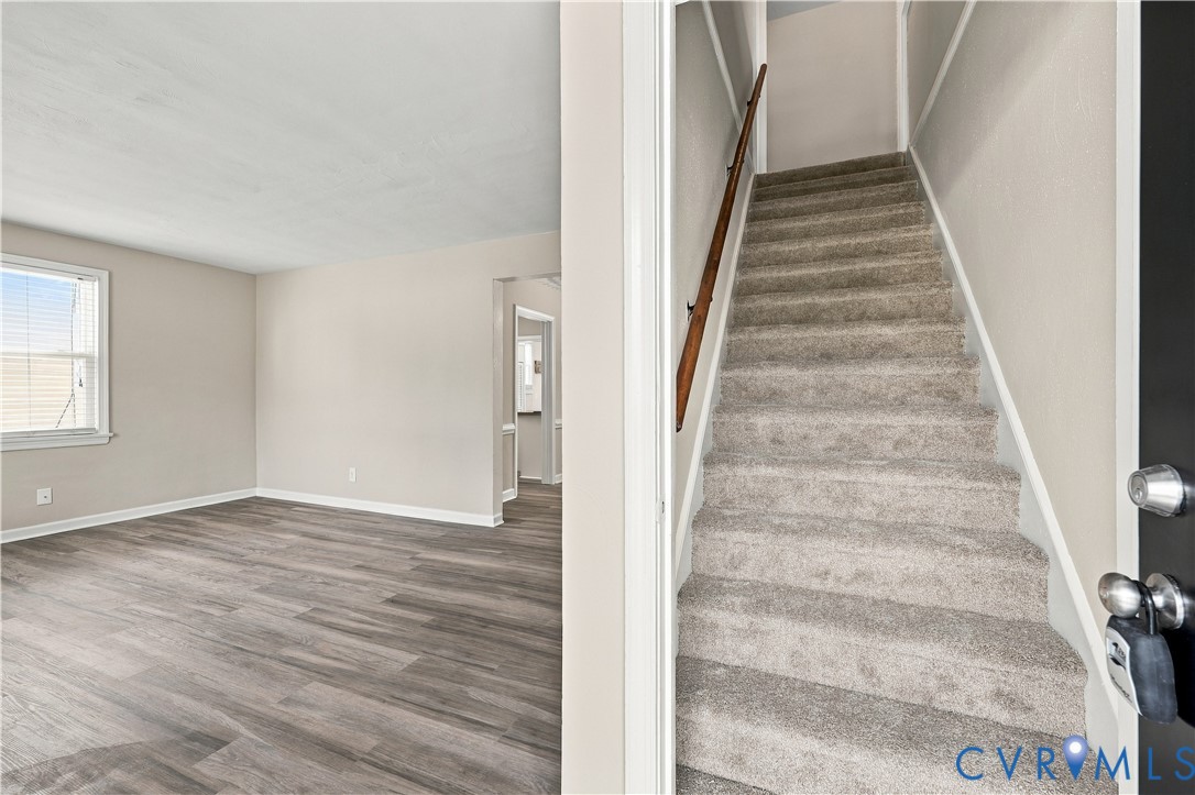 Wood-finish flooring, staircase with carpeted treads, wall-mounted wooden handrail, and neutral interior paint
