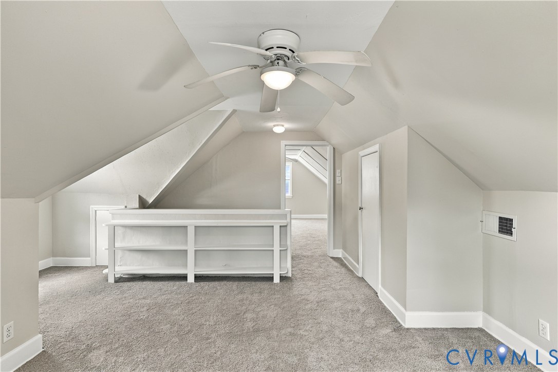Vaulted ceilings featuring a white-painted finish, built-in shelving unit, neutral carpet flooring, and a ceiling fan with integrated light fixture