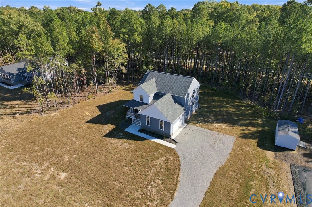 Two-story residence featuring grey lap siding, a shingled roof, a gravel driveway, and a detached storage shed on a wooded lot