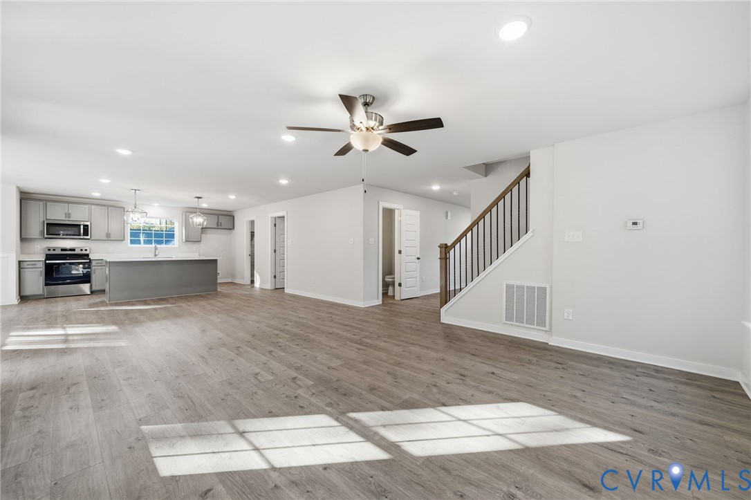 Open concept interior featuring wood-finish flooring, recessed lighting, a ceiling fan, and a kitchen equipped with cabinetry, a central island, and stainless-steel appliances