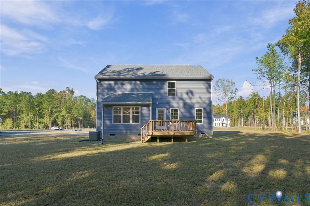 Rear exterior featuring gray vinyl siding, a wooden deck, multiple grid-pattern windows, a shingled roof, and a surrounding lawn with mature trees