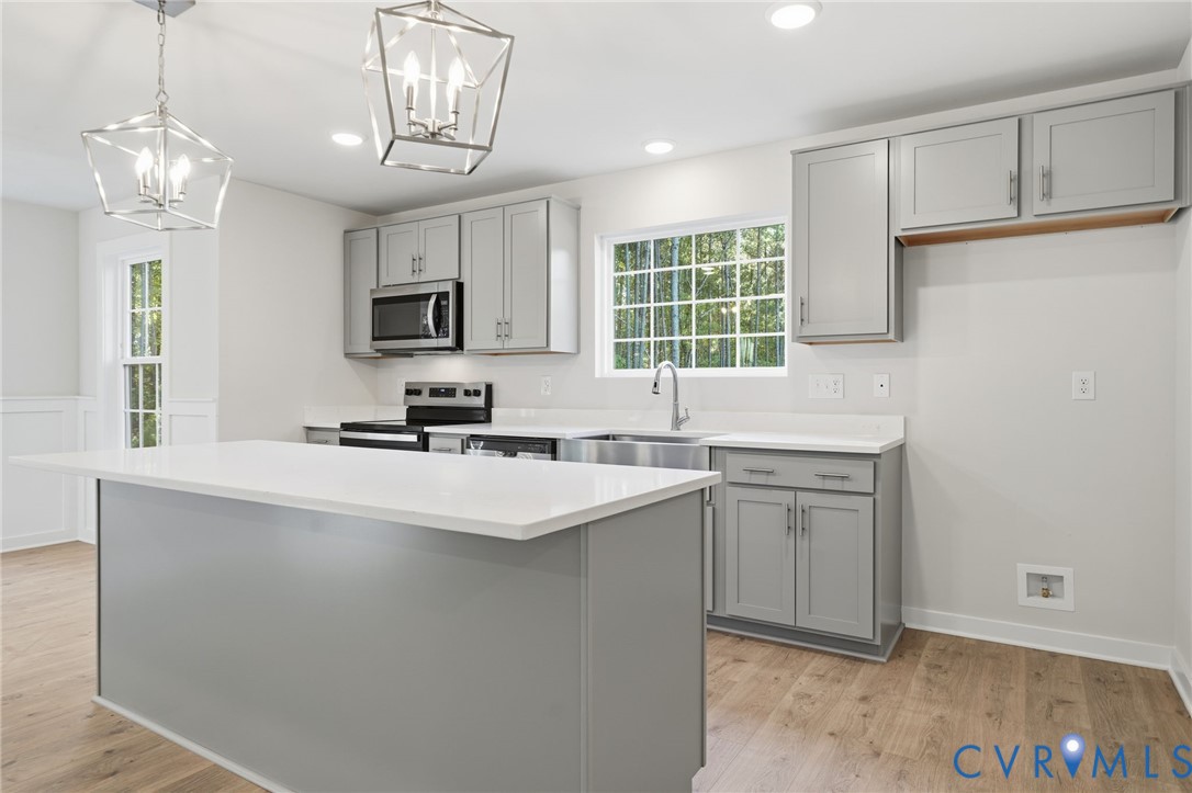 Kitchen featuring grey shaker-style cabinetry, quartz countertops, a central island, stainless steel appliances, and wood-finish flooring