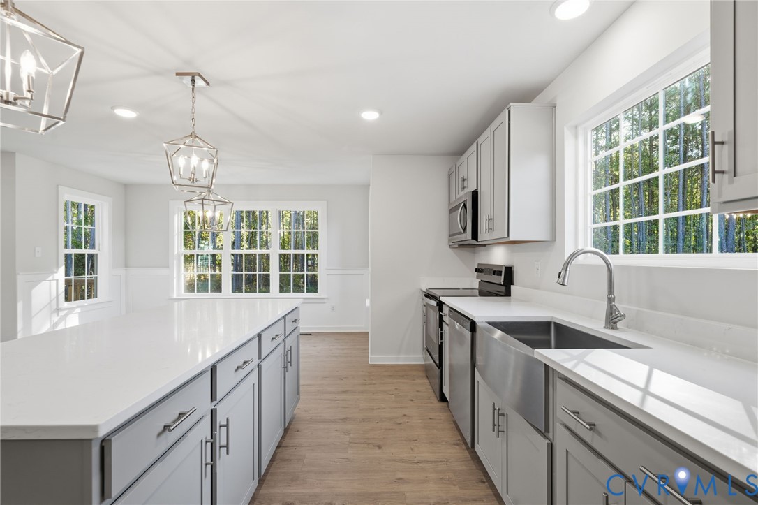 Kitchen featuring shaker-style cabinetry, quartz countertops, a stainless steel farmhouse sink, geometric pendant lighting, and wood-finish flooring