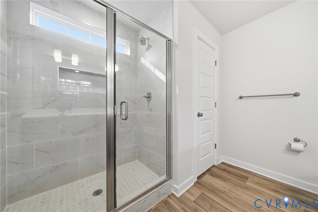 Walk-in shower featuring large-format stone-look wall tiles, a built-in recessed niche, clear glass enclosure, and wood-finish flooring