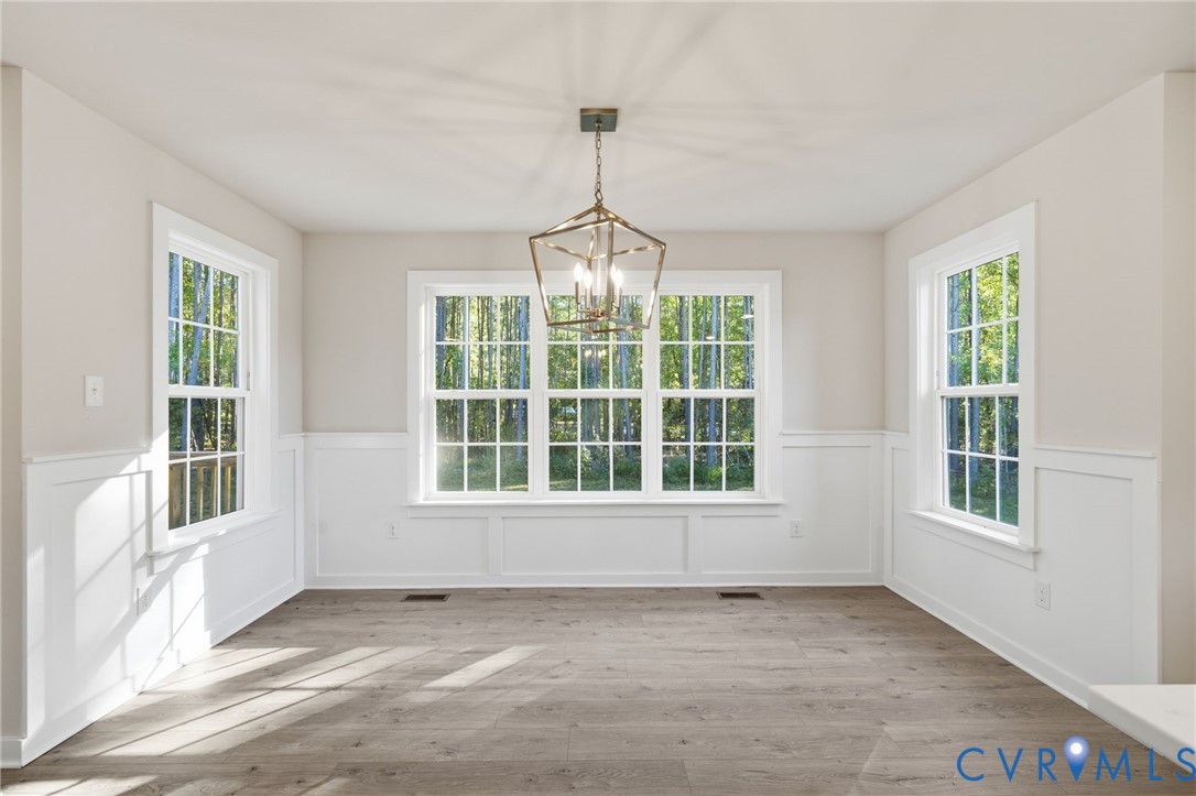 Room featuring wood-finish flooring, wainscoting, multi-pane windows, and a geometric chandelier