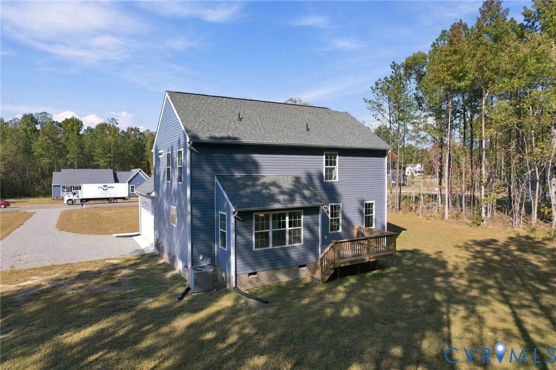 Two-story exterior featuring blue vinyl siding, an asphalt shingle roof, a rear wood deck, and a gravel driveway