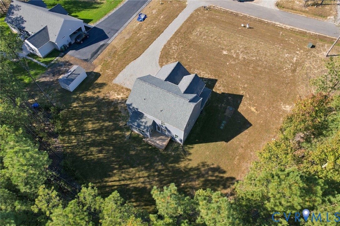 Aerial perspective of a detached residence featuring a multi-gable roofline, attached wooden deck, gravel driveway, and a partially wooded lot