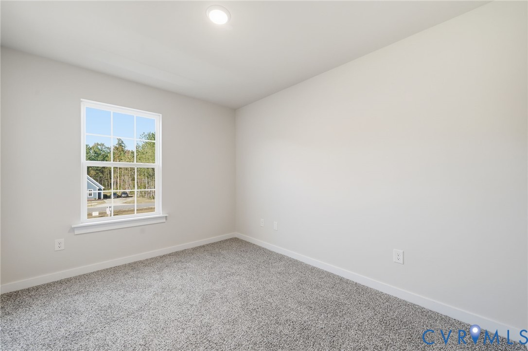 Neutral-toned interior space featuring light-colored wall paint, plush carpeting, a single recessed ceiling light, and a double-hung window with a grille pattern