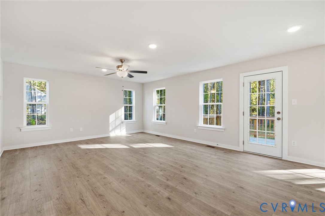 Open interior space featuring wood-finish flooring, recessed lighting, a ceiling fan with integrated light fixture, multiple multi-pane windows, and a glass-panel exterior door