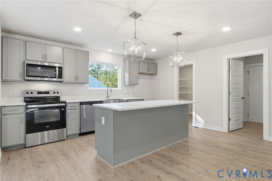 Kitchen featuring light gray cabinetry, quartz countertops, stainless steel appliances, a central island, and wood-finish flooring
