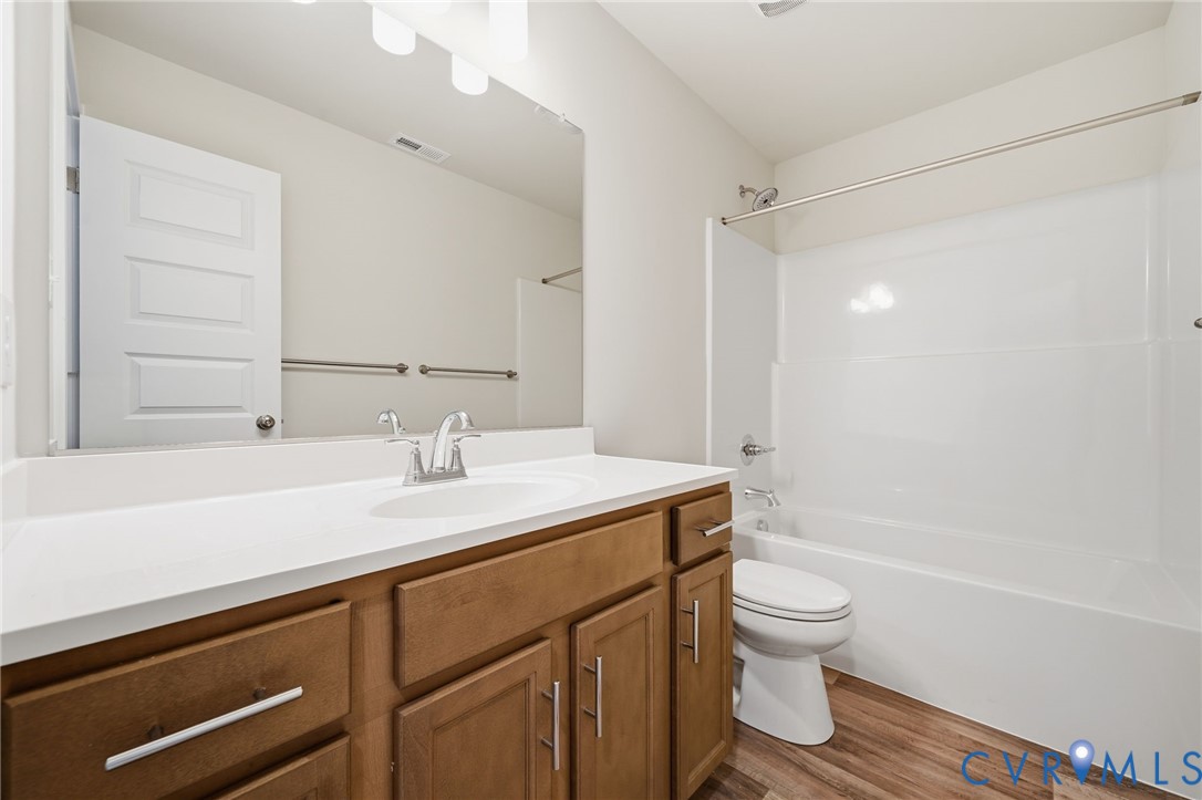 Bathroom featuring wood-finish cabinetry, a large integrated countertop vanity, full-width mirror, and a tub-shower combination with surround
