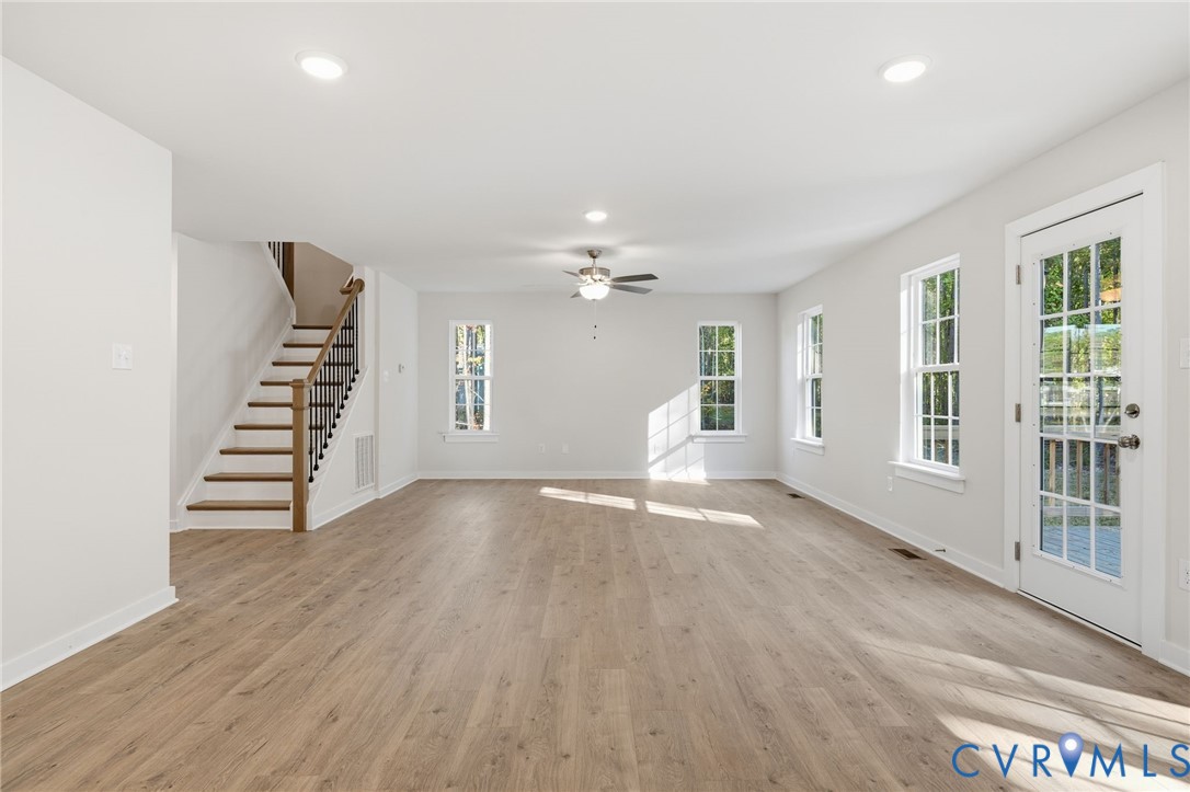 Open floor plan featuring wood-finish flooring, recessed lighting, ceiling fan, staircase with metal balusters, and a glass-paneled exterior door