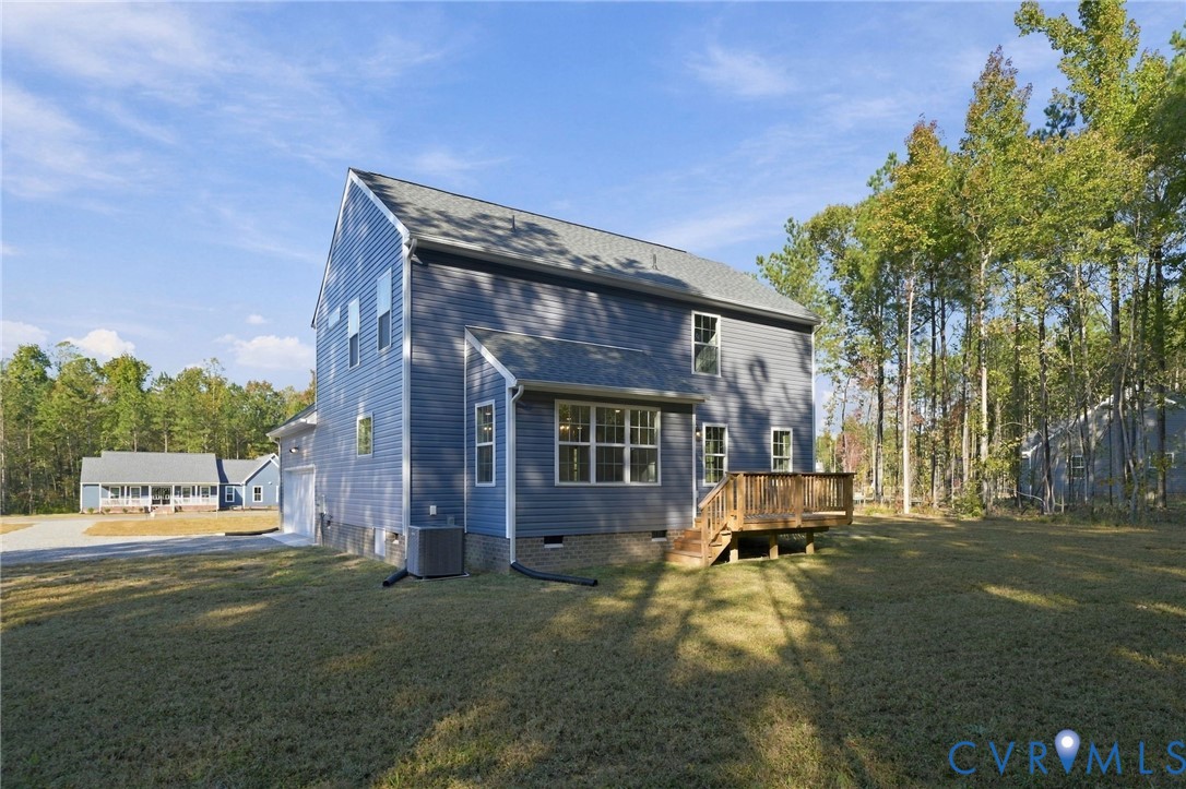 Two-story residence featuring blue horizontal siding, a gabled roof, an elevated wooden deck, and a grass-covered backyard surrounded by mature trees