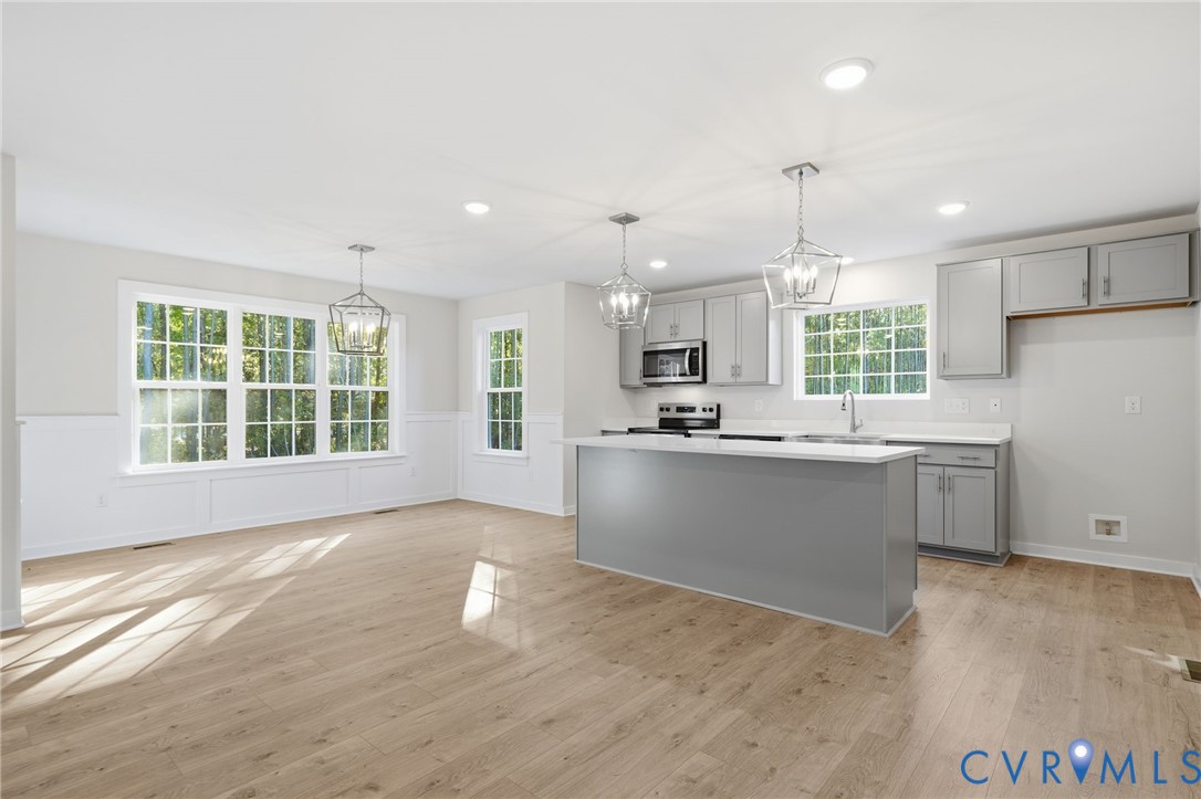 Kitchen featuring light grey shaker-style cabinetry, quartz countertops, a central island with integrated storage, wood-finish flooring, and multi-pane windows
