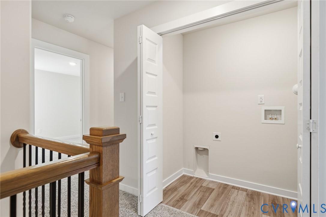 Laundry closet featuring wood-finish flooring, white bi-fold doors, and integrated utility hookups, complemented by wood-finish handrail and black metal balusters