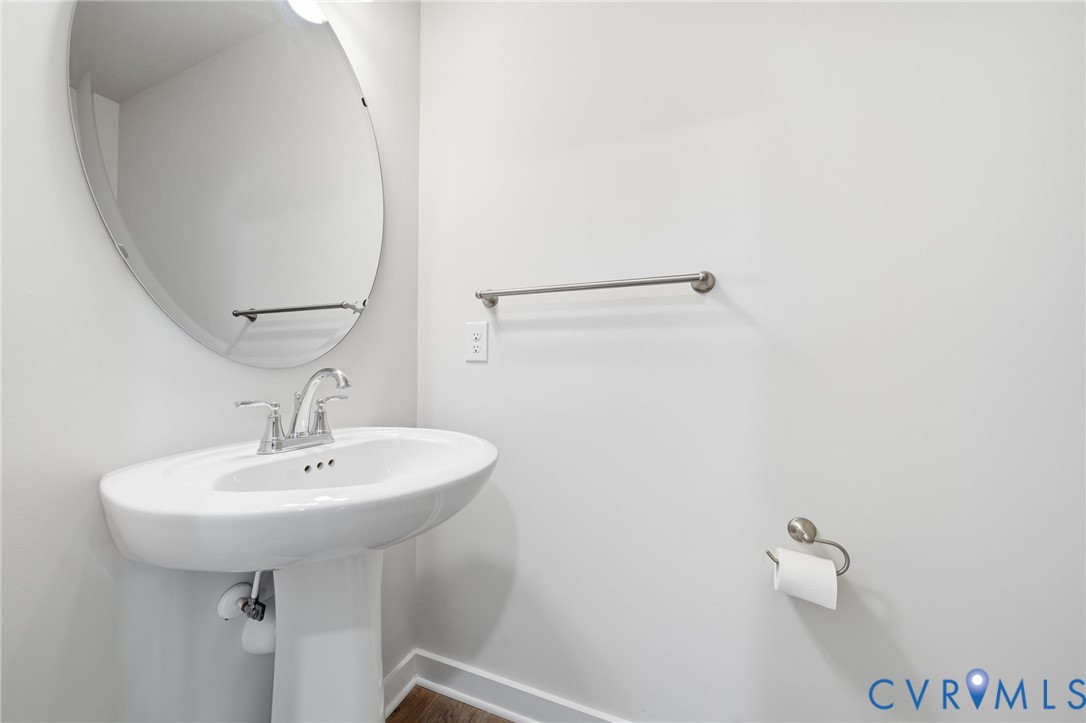 Oval wall-mounted mirror featuring a polished metal-finish faucet, pedestal sink, towel bar, and toilet paper holder