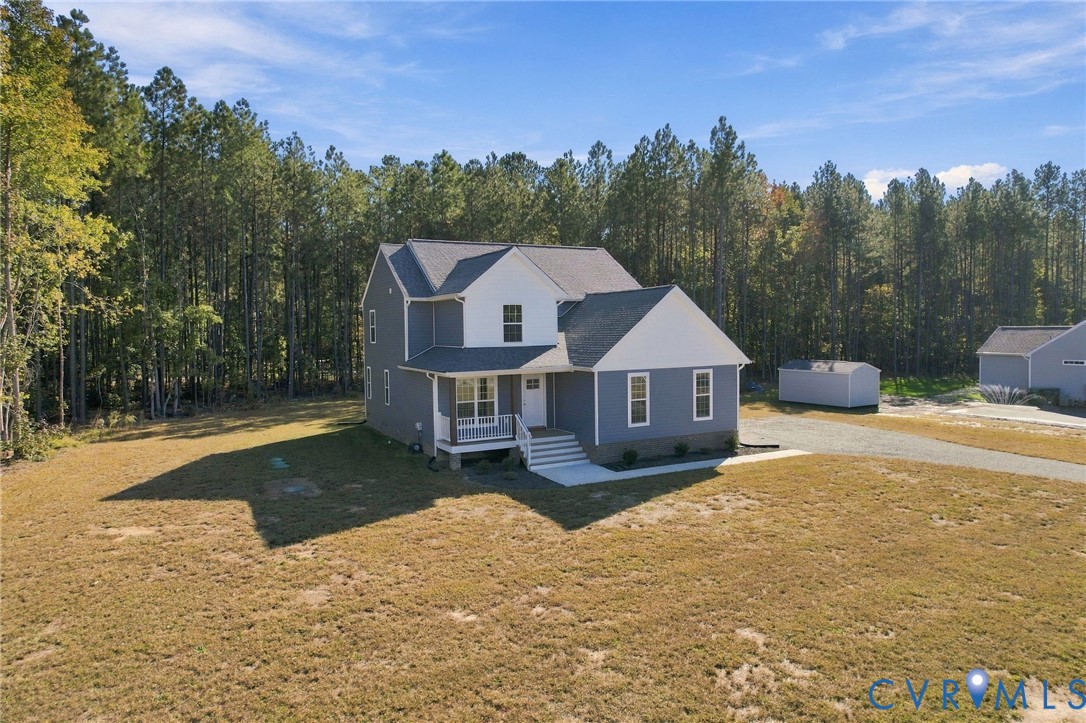 Two-story home featuring dual-tone siding, an attached front porch, stone foundation detailing, and an exterior storage structure on an expansive lot