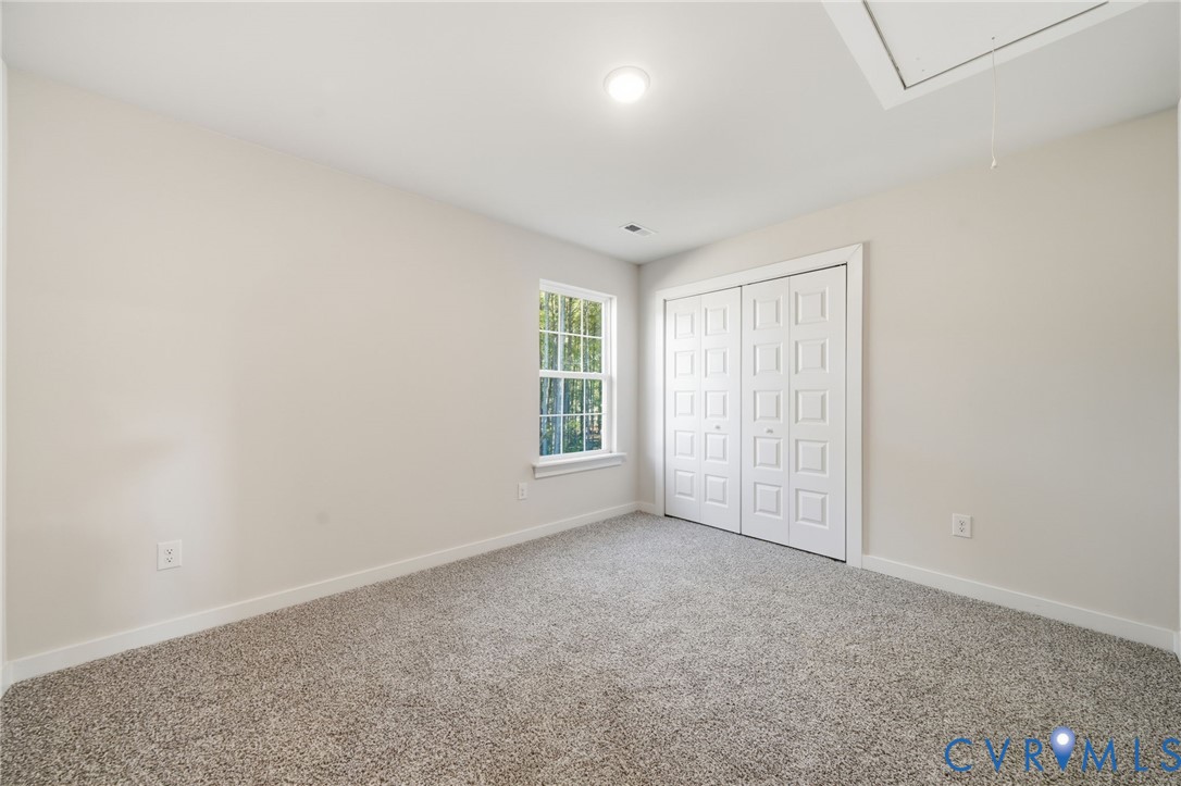 Neutral-toned interior space featuring neutral carpeting, a single-pane window, flush-mount lighting, and bi-fold closet doors with raised panels
