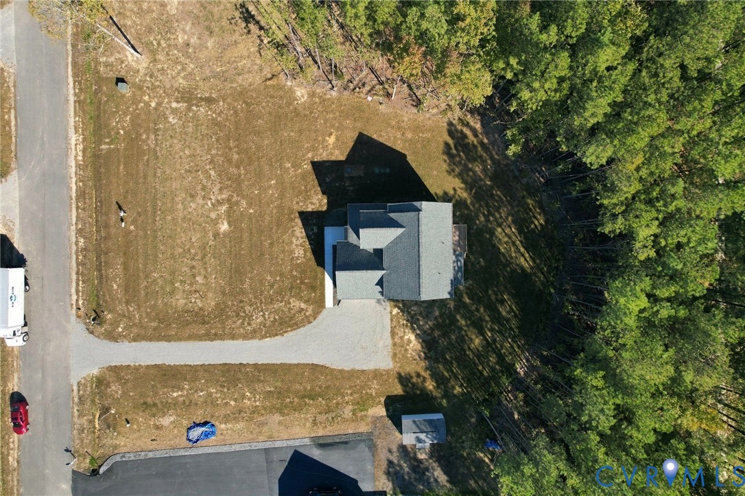 Aerial perspective of a detached residence featuring a gravel driveway, asphalt shingle roof, and expansive wooded lot perimeter