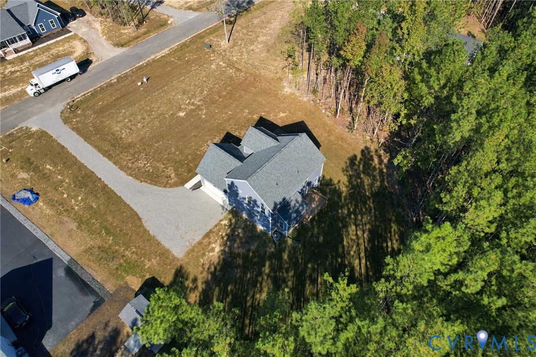 Aerial perspective of a detached residence featuring a multi-gabled roofline, light-colored siding, a gravel driveway, and a partially wooded lot