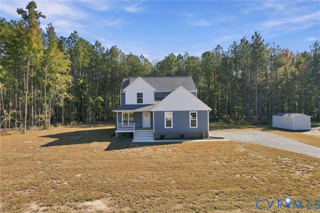 Two-story residence featuring a multi-gable roofline, front porch, gravel driveway, and detached storage structure