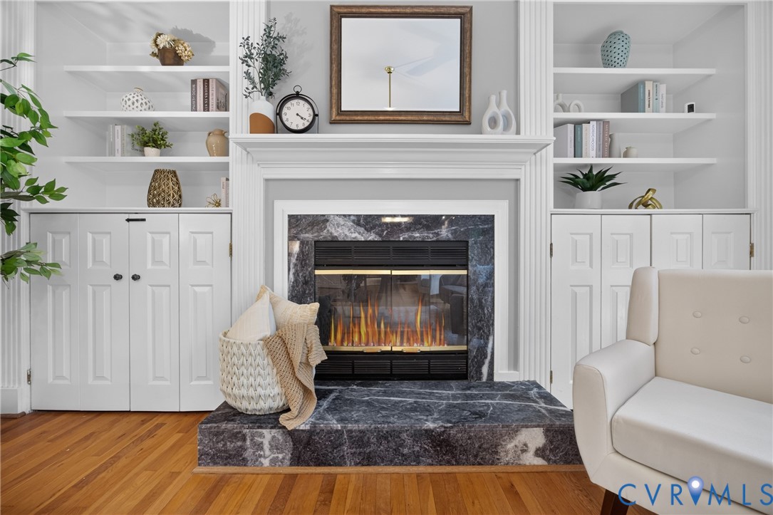 Fireplace featuring a stone surround and raised hearth, flanked by symmetrical built-in cabinetry with integrated shelving and base storage Fireplace featuring a stone surround and raised hearth, flanked by symmetrical built-in cabinetry with integrated shelving and base storage