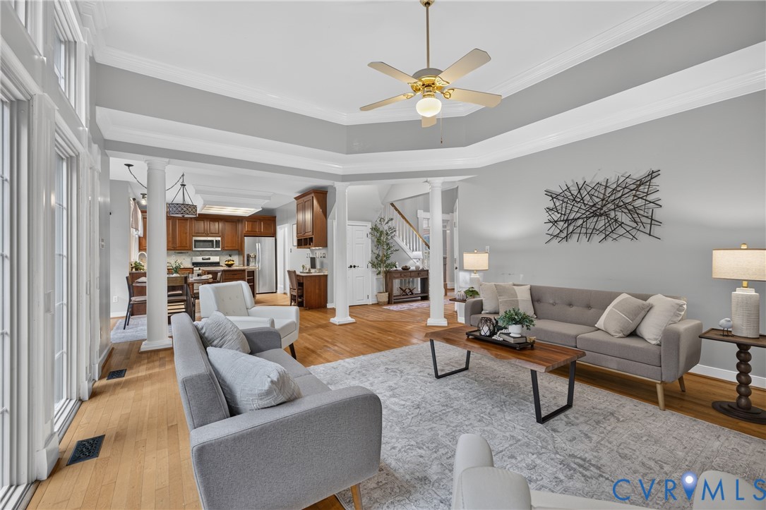 Open concept interior featuring wood flooring, a tray ceiling, structural columns, and large-paned windows