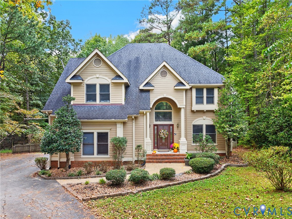Two-story exterior featuring tan horizontal siding, an arched entryway with decorative columns, multi-gabled roofline, and brick steps