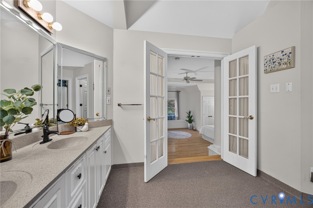 Double vanity with integrated sinks, neutral solid-surface countertops, multi-light vanity fixtures, and double glass-paneled French doors
