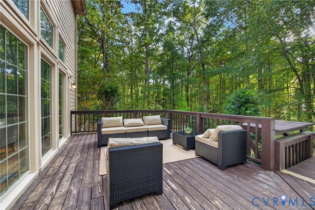 Elevated wood deck featuring a stained finish, custom-built integrated bench seating, and surrounding dark-toned wooden railings against a dense, mature forest backdrop