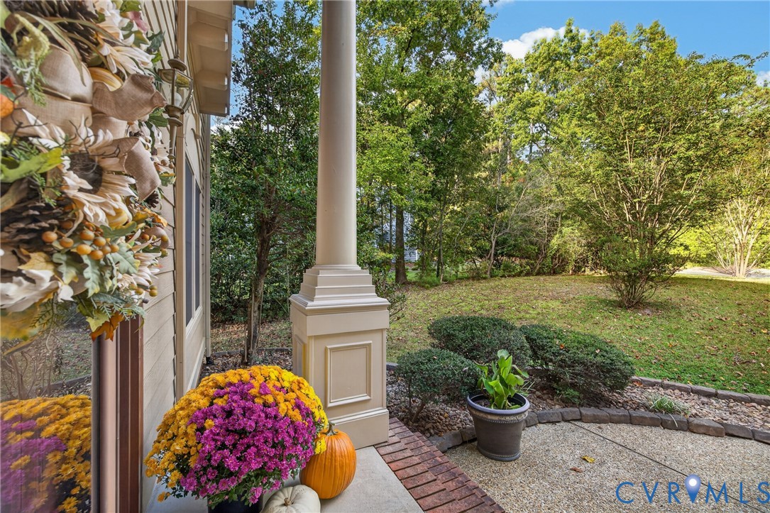 Covered porch featuring a paneled structural column, aggregate concrete flooring, and a brick border, opening to a grass-covered backyard with mature trees