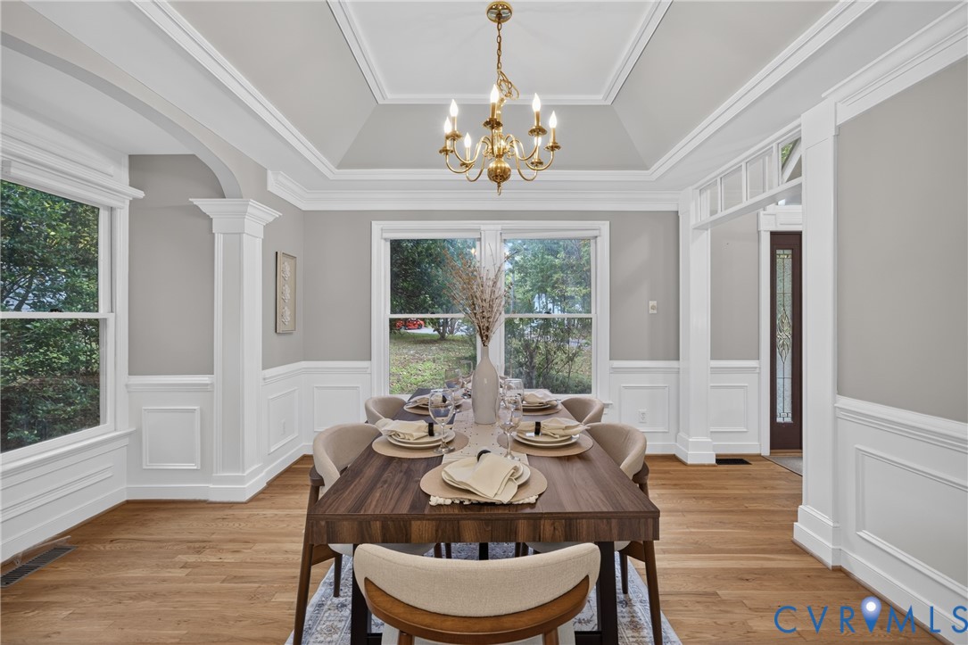 Tray ceiling with crown molding, wainscoting, wood-finish flooring, and brass-finish chandelier