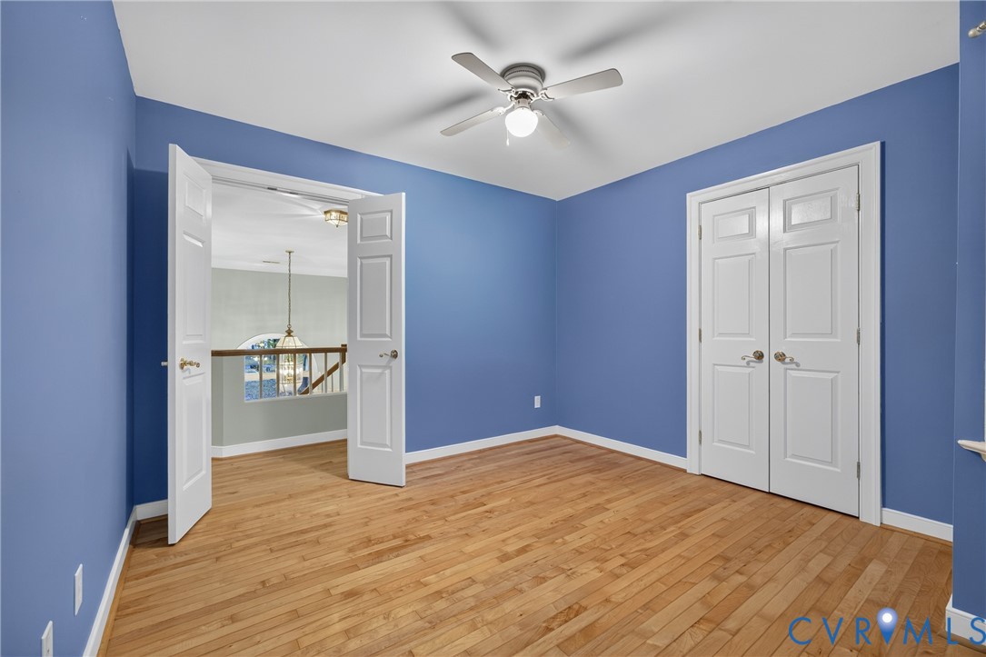Wood-finish flooring, white double-door closet, multi-panel doors, and ceiling fan with integrated lighting