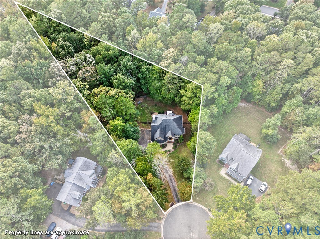 Aerial perspective of a multi-story residence situated on a wooded lot featuring an asphalt driveway and mature perimeter tree line