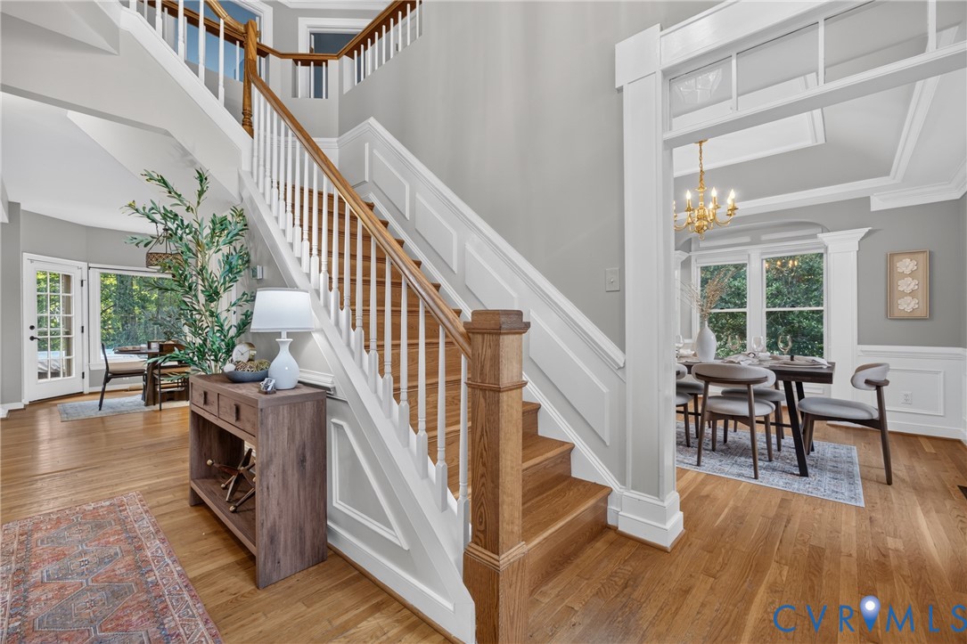 Foyer featuring a hardwood staircase with white balusters, wood-finish flooring, wainscoting, and crown molding Foyer featuring a hardwood staircase with white balusters, wood-finish flooring, wainscoting, and crown molding
