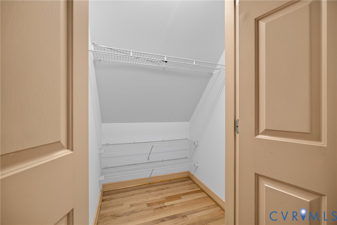 Storage closet featuring wood-finish flooring, two levels of white wire shelving, and paneled swinging doors