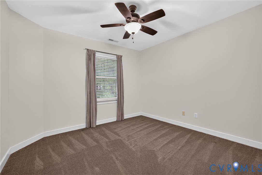 Neutral-toned interior featuring wall-to-wall carpeting, a multi-blade ceiling fan with an integrated light fixture, and a single-hung window
