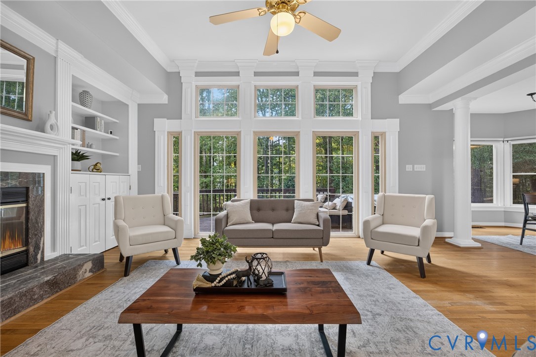 Vaulted ceilings featuring crown molding, floor-to-ceiling windows with grid detailing, built-in shelving, stone-surround fireplace, and wood-finish flooring Vaulted ceilings featuring crown molding, floor-to-ceiling windows with grid detailing, built-in shelving, stone-surround fireplace, and wood-finish flooring