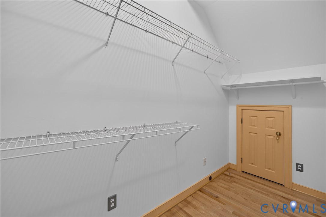 Storage area featuring wood-finish flooring, white walls, tiered wire shelving, and a natural wood-trim access door